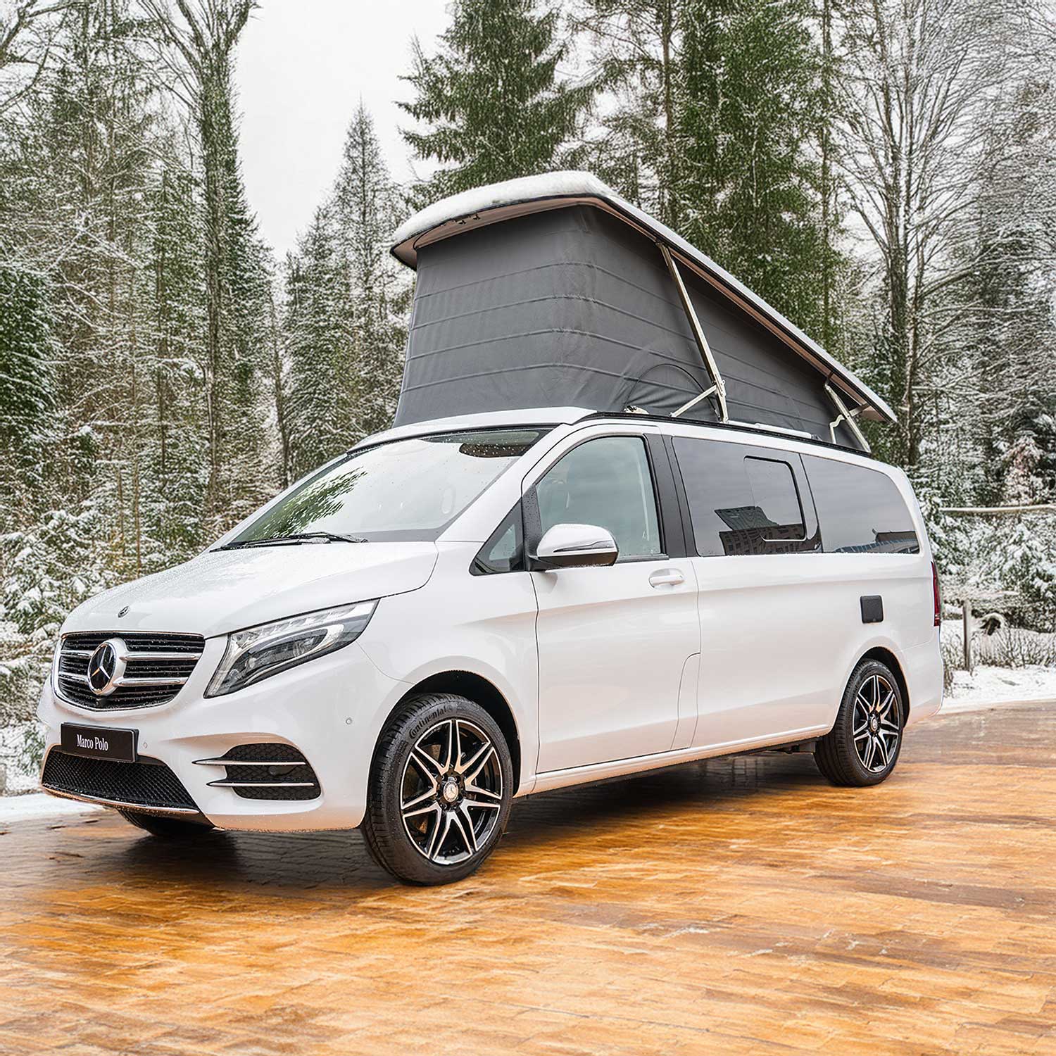 Ford Nugget steht vor einem winterlichen Wald mit schneebedeckten Bäumen und Tannen – Matratze 103x192 cm für Marco Polo Camping